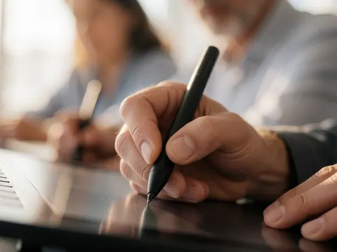 Gros plan d'une main utilisant un stylet sur une tablette pour créer des dessins, avec un arrière-plan flou suggérant un environnement de travail créatif.