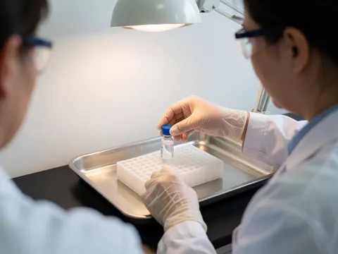 Technicien en laboratoire clinique déposant un échantillon dans un rack blanc stérile sur un plateau en acier inoxydable sous un éclairage de travail.