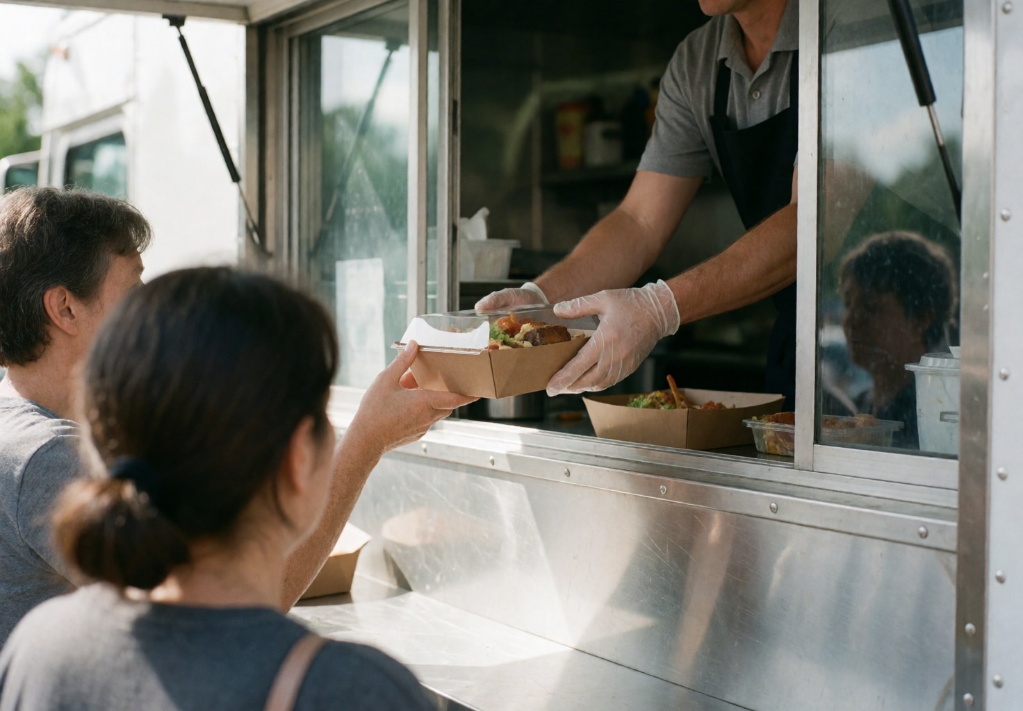 Une main portant un gant de protection remet une boîte de repas à un client depuis un camion de restauration rapide, illustrant un service hygiénique et efficace.