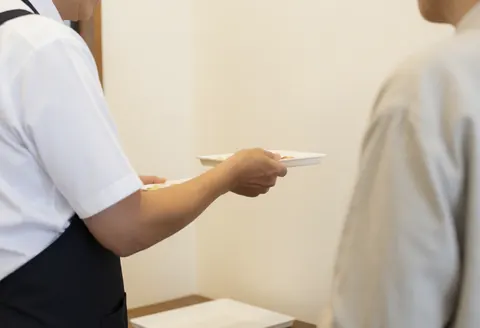 Un employé portant un tablier sert de la nourriture à un client dans un local aux murs blancs.