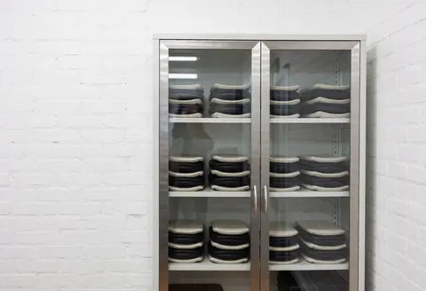 Cabinet métallique contenant des équipements de thérapies thermiques dans un studio de physiothérapie aux murs de briques blanches et à l'éclairage clinique lumineux.