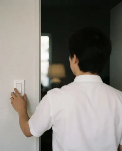 Un professionnel en chemise blanche règle un interrupteur sur un mur clair, dans un intérieur au éclairage tamisé.