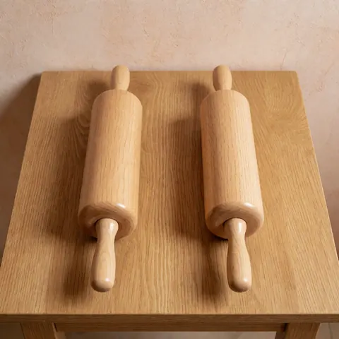 Deux rouleaux à pâtisserie en bois poli posés sur une table en bois clair devant un mur terracotta, éclairage naturel, style minimaliste adapté à la boulangerie et la pâtisserie