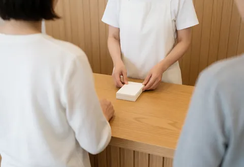 Un professionnel en tablier blanc range des cartes de rendez-vous sur une table en bois dans un espace d'accueil client avec des murs en planches.