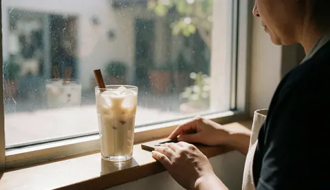 Un verre de boisson horchata à la cannelle posé sur un rebord de fenêtre baigné de lumière solaire naturelle, créant une ambiance chaleureuse et rafraîchissante pour une maison d'hôtes.