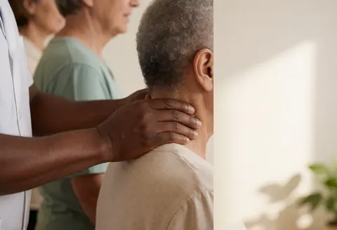 Thérapeute effectuant un massage du cou d'un client dans une salle de massage avec un mur blanc et une lumière naturelle.