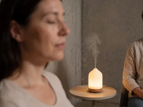 Femme enceinte au calme avec un diffuseur d'huiles essentielles sur un mur en béton, évoquant le bien-être prénatal et la relaxation.