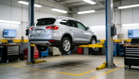 Un véhicule suv argenté surélevé sur un pont élévateur hydraulique dans un garage automobile avec des outils et des lignes de sécurité au sol.