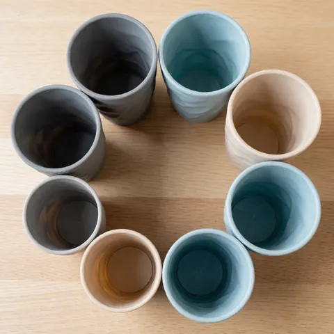 Des gobelets en silicone réutilisables sont disposés en cercle sur une surface en bois clair, avec des tons neutres et une texture flexible, idéal pour un menu ou un catalogue de produits.