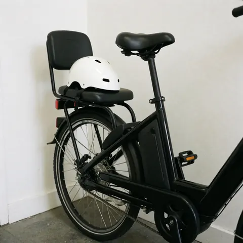 Vélo électrique de taxi noir avec siège passager et casque blanc, appuyé contre un mur blanc, prêt pour le service.