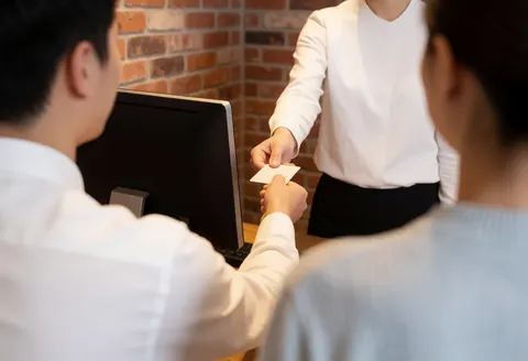 Un employé dans un bureau avec un mur en briques remet une carte à un client, illustrant un service en action.