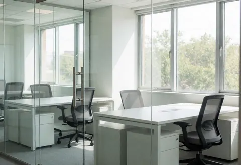 Espace de travail vide avec tables blanches, chaises noires et grandes fenêtres laissant entrer la lumière naturelle.