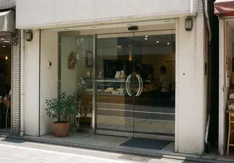 Entrée de local avec porte vitrée et plante en pot, murs blancs et reflets sur le verre