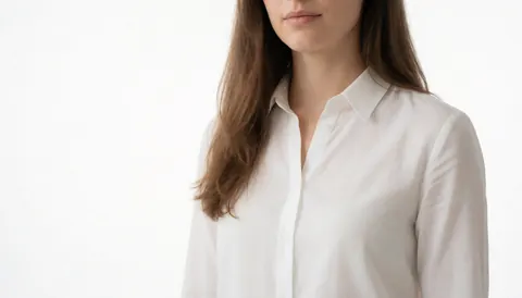 Portrait de profil d'une femme aux cheveux châtains portant une chemise blanche sur fond blanc uni, idéal pour les sites web professionnels.