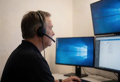 Un opérateur de sécurité équipé d'un casque travaille devant trois écrans dans une salle de contrôle aux murs clairs et à l'ambiance professionnelle.