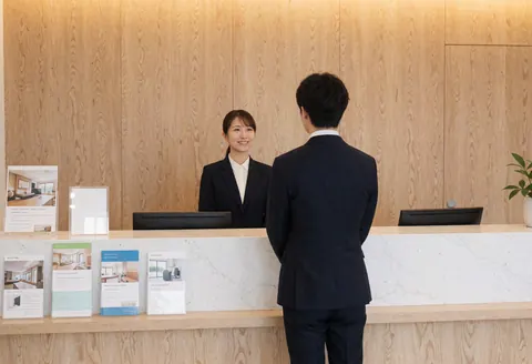 Accueil d'académie de langues avec réceptionniste souriante et client, brochures et ordinateur sur comptoir en bois clair.