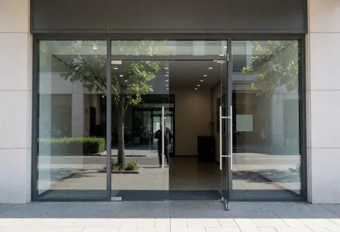 Entrée d'un local moderne avec portes vitrées, reflets d'arbres et intérieur lumineux, idéal pour tout type de commerce.