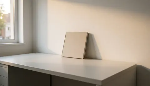 Album de photos posé sur un bureau blanc, éclairé par la lumière naturelle d'une fenêtre, sur un fond blanc minimaliste, idéal pour un photographe de mariage.