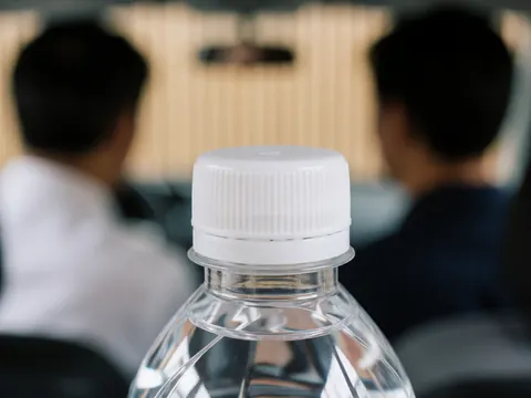 Gros plan sur le bouchon d'une bouteille d'eau avec une texture visible, sur un fond flou montrant deux personnes et des murs en bois clair, idéal pour illustrer la propreté ou l'hygiène.
