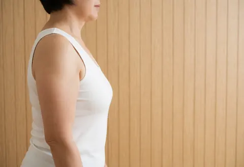 Profil d'une femme vêtue d'une chemise blanche se tenant devant un mur en bois avec un fond épuré et une lumière naturelle.