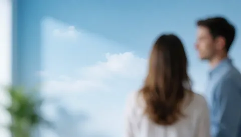 Vue d'un ciel bleu et nuageux à travers une fenêtre d'un bureau moderne baigné de lumière naturelle, servant de fond neutre et professionnel.