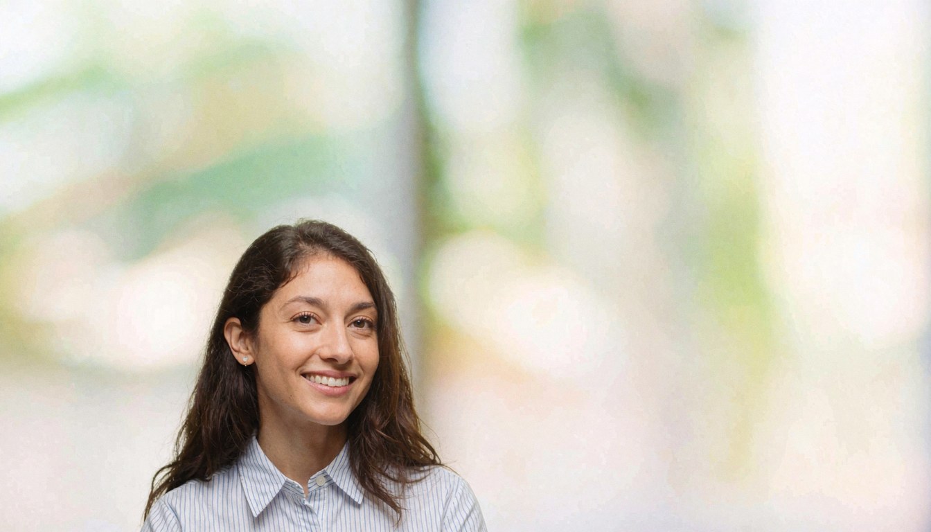 Portrait d'une femme souriante vêtue d'une chemise blanche, dans un environnement de bureau avec un arrière-plan flou, évoquant le monde des affaires.
