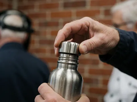 Main adulte ouvrant une bouteille d'eau réutilisable en métal avec des gouttes, fond de mur en briques, scène de détail pour entreprise de zoo.