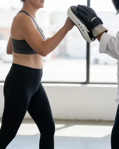 Une femme en tenue de sport effectue un mouvement de jab avec un gant de boxe dans un studio éclairé par la lumière naturelle sur un sol en béton.