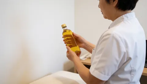 Vue de dos d'un professionnel tenant une bouteille d'huile dans une clinique ayurvédique à fond blanc avec espace pour texte