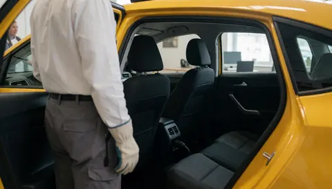 Intérieur d'un taxi jaune avec porte ouverte, conducteur dos tourné et client assis, espace propre et moderne pour services de transport.