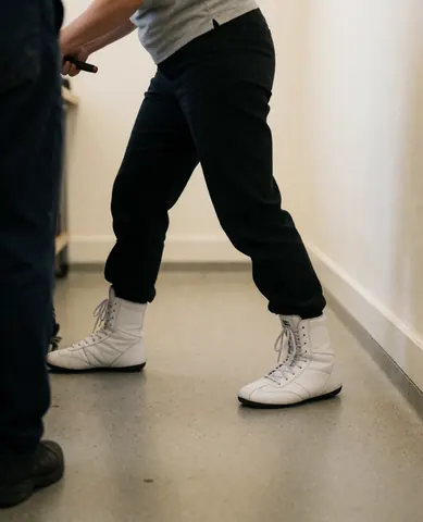 Chaussures de boxe blanches en position d'entraînement, cliente en séance, murs chauds, sol en caoutchouc, ambiance de gymnase.