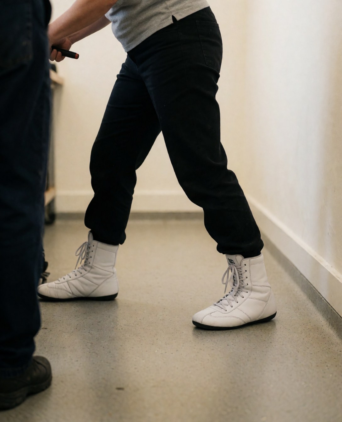 Chaussures de boxe blanches en position d'entraînement, cliente en séance, murs chauds, sol en caoutchouc, ambiance de gymnase.