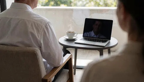 Une cliente est assise sur le balcon d'un apart-hôtel, profitant de la vue extérieure avec son ordinateur portable et une tasse de café.