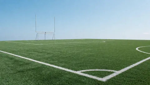 Terrain de football américain vide avec lignes blanches et poteaux de but sous un ciel bleu clair, idéal pour un entraînement en extérieur.