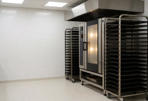 Four de convection industriel dans une boulangerie, accompagné de racks pour plaques et de murs carrelés blancs, prêt pour la cuisson.