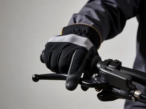 Gros plan d'une main portant un gant noir et gris saisissant fermement le guidon d'un vélo sur fond de mur gris uni.
