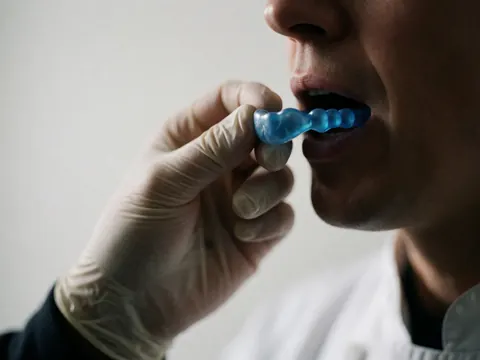 Instructeur de boxe portant un gant blanc ajuste un protège-dents bleu dans sa bouche sur fond blanc, geste de protection.
