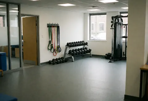 Salle d'entraînement équipée de bandes de résistance, d'un rack de poids et d'une machine à câbles, idéale pour la rééducation et le travail fonctionnel.