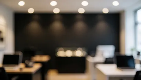 Fond de bureau moderne avec mur sombre, tables et ordinateurs portables, lumières de plafond en bokeh, idéal pour texte.