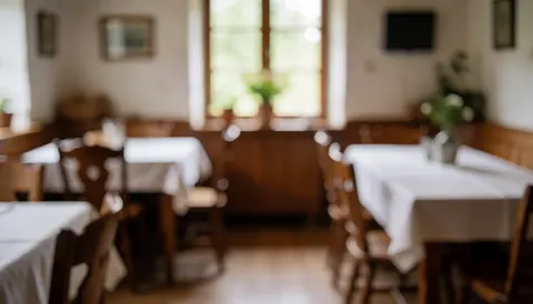 Intérieur d'un restaurant rural avec tables couvertes de nappes blanches, chaises en bois et lumière naturelle entrant par la fenêtre, idéal pour fond de texte.