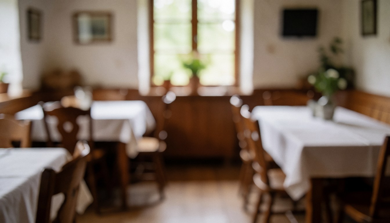 Intérieur d'un restaurant rural avec tables couvertes de nappes blanches, chaises en bois et lumière naturelle entrant par la fenêtre, idéal pour fond de texte.