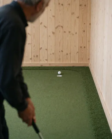 Vue arrière d'une cliente se préparant à frapper une balle avec un putter sur un simulateur de golf doté de murs en bois.