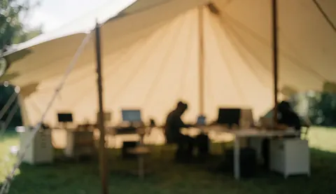 Tente beige abritant des tables de travail équipées d'ordinateurs, servant de fond neutre pour du texte lors d'événements en plein air.