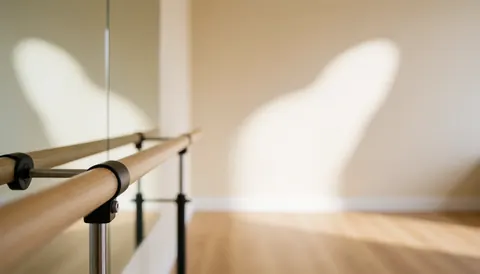 Barre de ballet en bois dans un studio de danse avec murs beige, sol en bois clair, lumière naturelle et miroir, idéal pour textes.