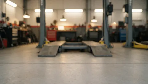 Vue d'un ascenseur pour véhicules dans un garage avec murs blancs et sol en béton, éclairage professionnel, fond neutre adapté pour textes sur les services de réparation automobile.