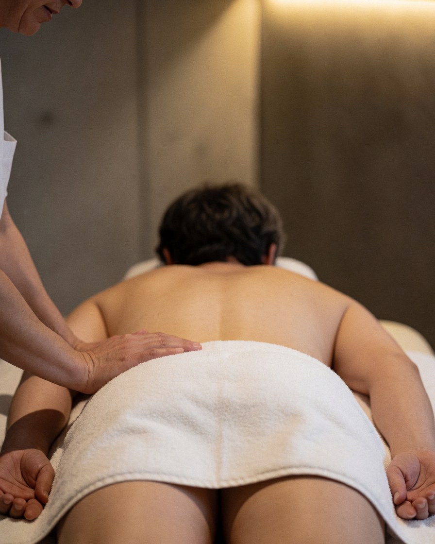Un thérapeute pratique un massage des tissus profonds sur le dos d'un client allongé dans une salle avec des murs en béton et une lumière chaude.