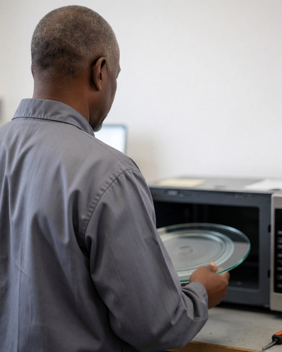 Technicien de réparation installant un nouveau plateau en verre dans un micro-ondes ouvert au sein d'un atelier aux murs blancs.