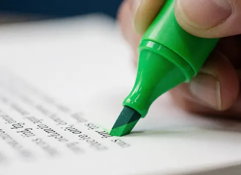 Main tenant un marqueur vert à pointe feutre sur un document papier blanc avec du texte, sur fond bleu foncé, détail de papeterie.