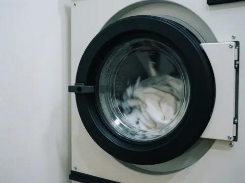 Vue d'une laveuse industrielle en marche avec du linge blanc et de l'eau, sur un fond blanc, adaptée pour un hostel.