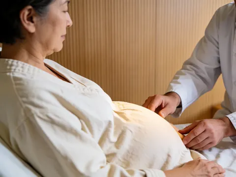 Mains d'un praticien reiki posées sur le ventre d'une cliente enceinte, dans un cadre en bois clair avec une lumière chaleureuse évoquant le bien-être.